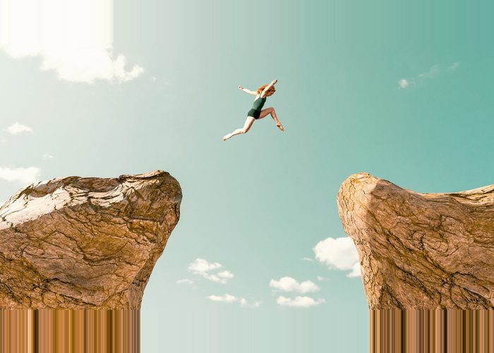 Woman makes dangerous jump between two rock formations.